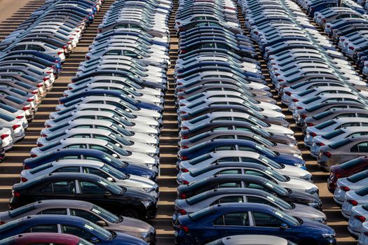 Rows of a new cars parked in a distribution center on a car factory on a sunny day. Top view to the parking in the open air.