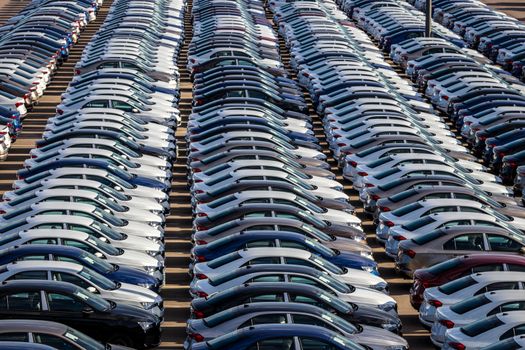 Rows of a new cars parked in a distribution center on a car factory on a sunny day. Parking in the open air.