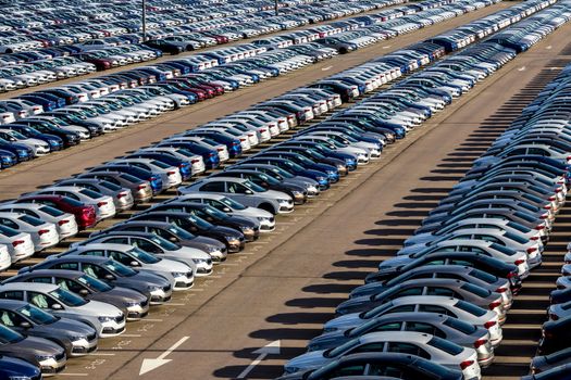 Rows of a new cars parked in a distribution center on a car factory on a sunny day. Top view to the parking in the open air.