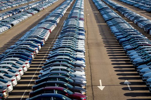 Rows of a new cars parked in a distribution center on a car factory on a sunny day. Top view to the parking in the open air.