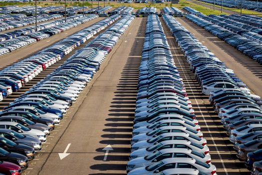 Rows of a new cars parked in a distribution center on a car factory on a sunny day. Top view to the parking in the open air.