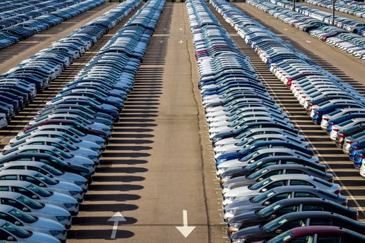 Rows of a new cars parked in a distribution center on a car factory on a sunny day. Parking in the open air.