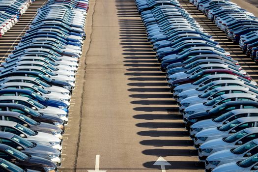 Rows of a new cars parked in a distribution center on a car factory on a sunny day. Top view to the parking in the open air.