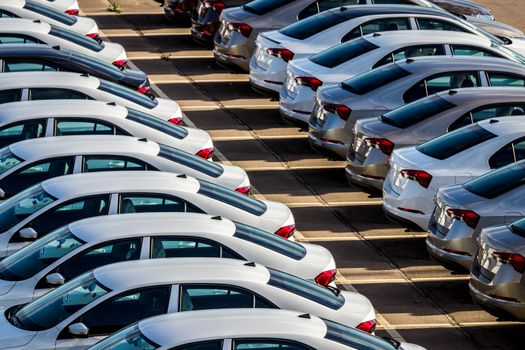 Rows of a new cars parked in a distribution center on a car factory on a sunny day. Top view to the parking in the open air.