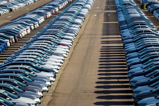 Rows of a new cars parked in a distribution center on a car factory on a sunny day. Top view to the parking in the open air.