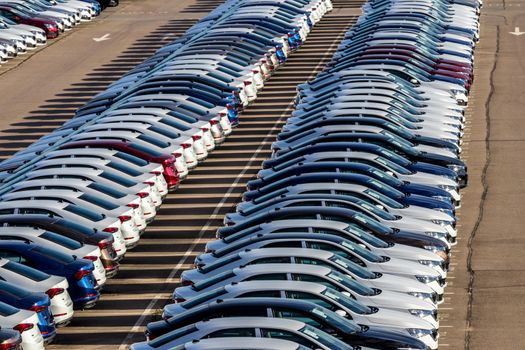 Rows of a new cars parked in a distribution center on a car factory on a sunny day. Top view to the parking in the open air.