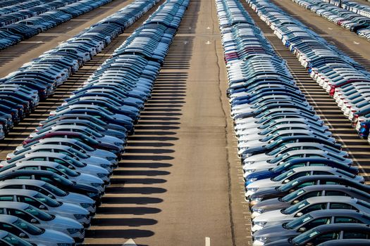 Rows of a new cars parked in a distribution center on a car factory on a sunny day. Parking in the open air.