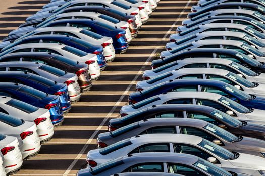 Rows of a new cars parked in a distribution center on a car factory on a sunny day. Top view to the parking in the open air.