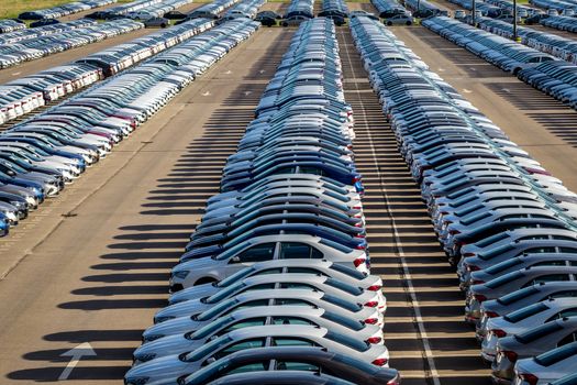 Rows of a new cars parked in a distribution center on a car factory on a sunny day. Top view to the parking in the open air.