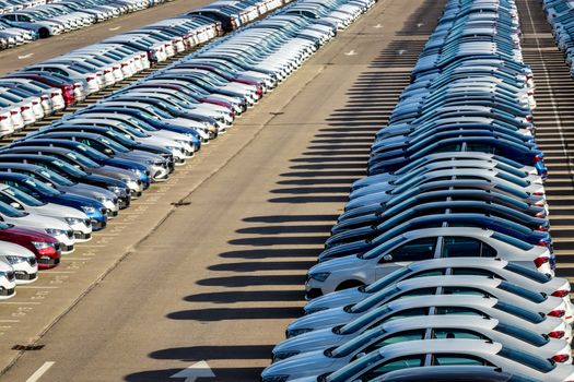 Rows of a new cars parked in a distribution center on a car factory on a sunny day. Top view to the parking in the open air.