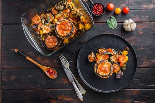 Served portobello mushrooms,baked and stuffed with cheddar cheese, cherry tomatoes and sage on black plate over old wooden dark background top view.