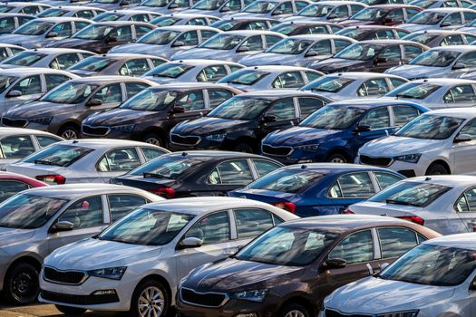 Rows of a new cars parked in a distribution center on a car factory on a sunny day. Parking in the open air.