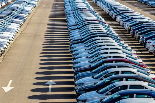 Rows of a new cars parked in a distribution center on a car factory on a sunny day. Top view to the parking in the open air.