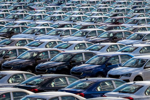 Rows of a new cars parked in a distribution center on a car factory on a sunny day. Parking in the open air.