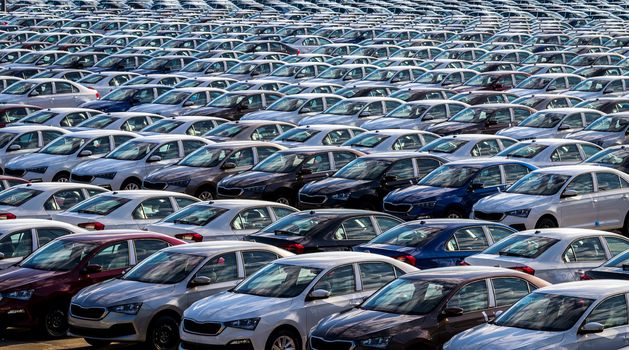 Rows of a new cars parked in a distribution center on a car factory on a sunny day. Top view to the parking in the open air.