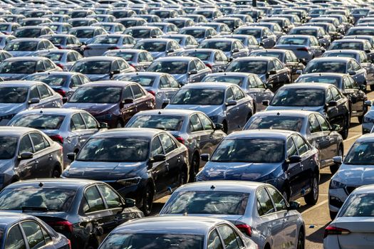 Rows of a new cars parked in a distribution center on a car factory on a sunny day. Parking in the open air.