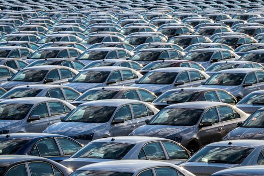 Rows of a new cars parked in a distribution center on a car factory on a sunny day. Parking in the open air.
