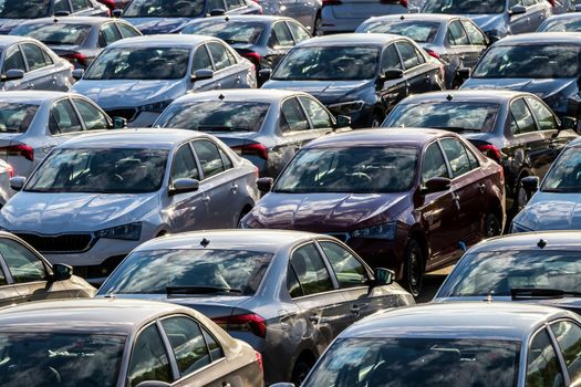 Rows of a new cars parked in a distribution center on a car factory on a sunny day. Top view to the parking in the open air.