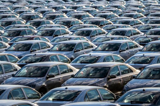 Rows of a new cars parked in a distribution center on a car factory on a sunny day. Top view to the parking in the open air.