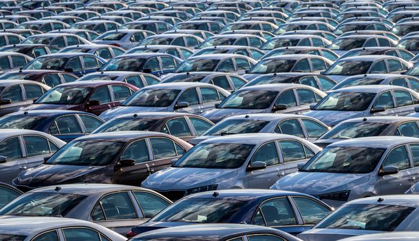 Rows of a new cars parked in a distribution center on a car factory on a sunny day. Top view to the parking in the open air.