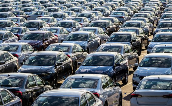 Rows of a new cars parked in a distribution center on a car factory on a sunny day. Top view to the parking in the open air.