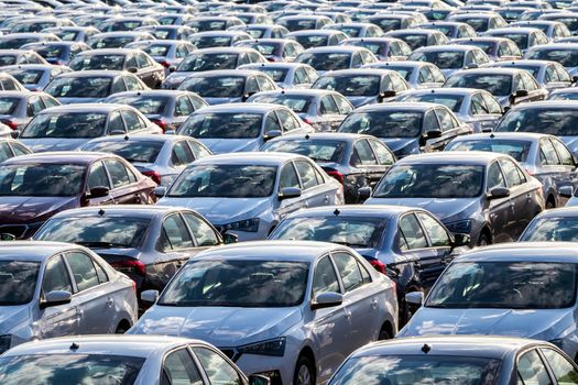 Rows of a new cars parked in a distribution center on a car factory on a sunny day. Top view to the parking in the open air.