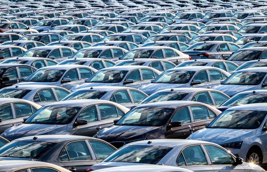 Rows of a new cars parked in a distribution center on a car factory on a sunny day. Top view to the parking in the open air.