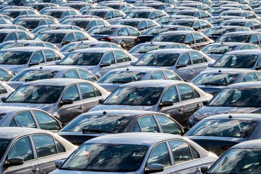 Rows of a new cars parked in a distribution center on a car factory on a sunny day. Top view to the parking in the open air.