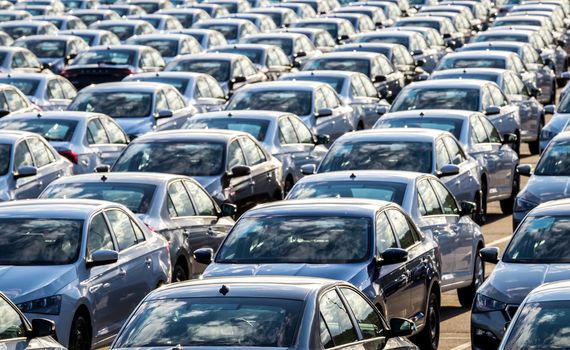 Rows of a new cars parked in a distribution center on a car factory on a sunny day. Parking in the open air.