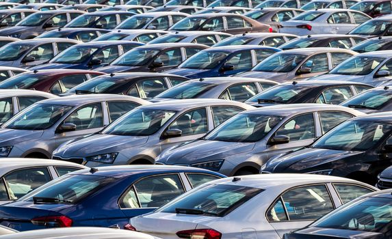 Rows of a new cars parked in a distribution center on a car factory on a sunny day. Parking in the open air.