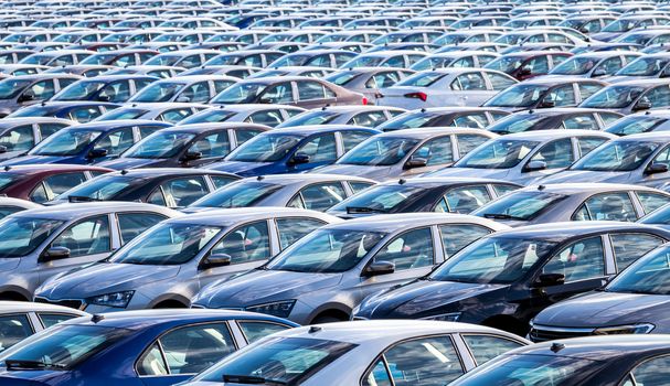 Rows of a new cars parked in a distribution center on a car factory on a sunny day. Top view to the parking in the open air.