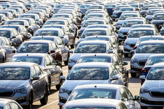 Rows of a new cars parked in a distribution center on a car factory on a sunny day. Top view to the parking in the open air.