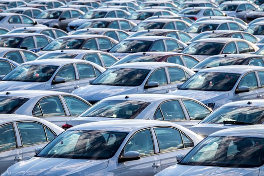 Rows of a new cars parked in a distribution center on a car factory on a sunny day. Parking in the open air.