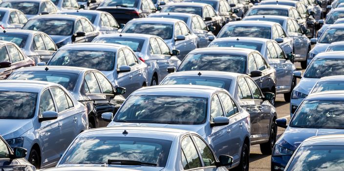 Rows of a new cars parked in a distribution center on a car factory on a sunny day. Top view to the parking in the open air.