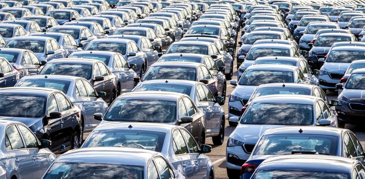 Rows of a new cars parked in a distribution center on a car factory on a sunny day. Parking in the open air.