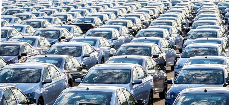 Rows of a new cars parked in a distribution center on a car factory on a sunny day. Top view to the parking in the open air.