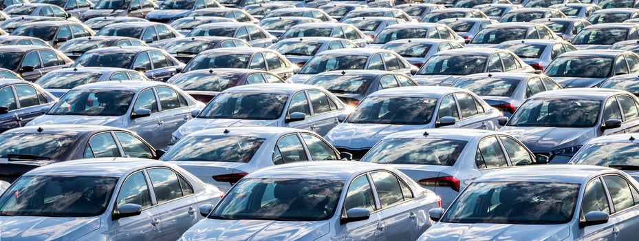 Rows of a new cars parked in a distribution center on a car factory on a sunny day. Top view to the parking in the open air.