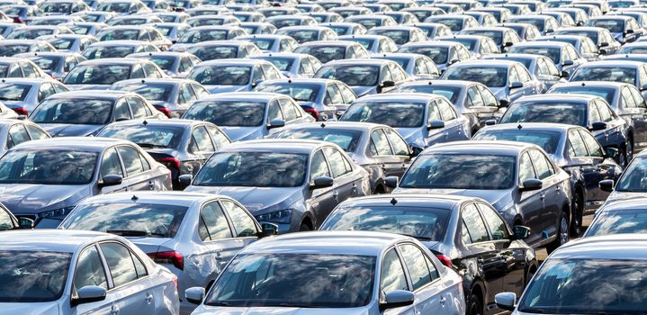 Rows of a new cars parked in a distribution center on a car factory on a sunny day. Top view to the parking in the open air.