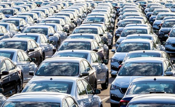 Rows of a new cars parked in a distribution center on a car factory on a sunny day. Top view to the parking in the open air.