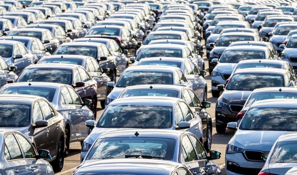 Rows of a new cars parked in a distribution center on a car factory on a sunny day. Top view to the parking in the open air.