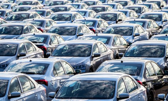 Rows of a new cars parked in a distribution center on a car factory on a sunny day. Parking in the open air.