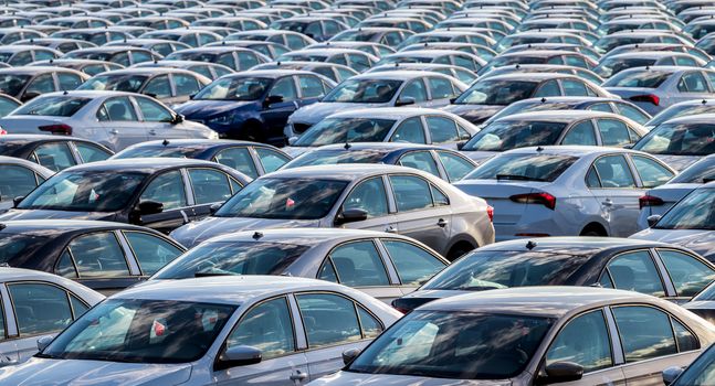 Rows of a new cars parked in a distribution center on a car factory on a sunny day. Parking in the open air.