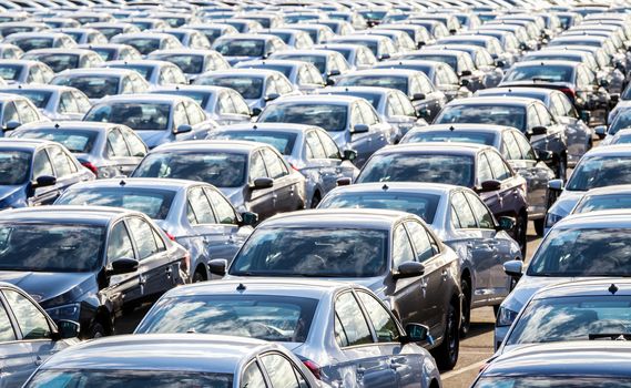 Rows of a new cars parked in a distribution center on a car factory on a sunny day. Top view to the parking in the open air.