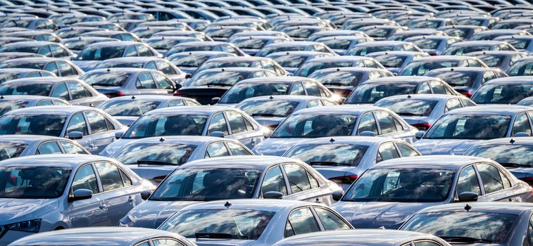 Rows of a new cars parked in a distribution center on a car factory on a sunny day. Parking in the open air.