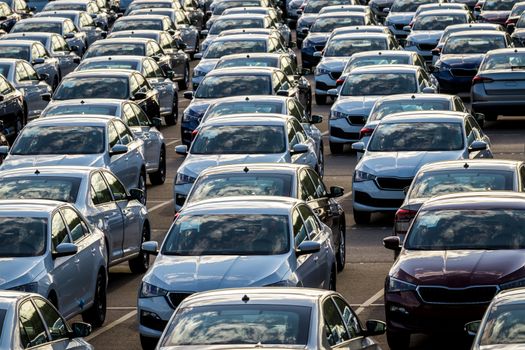 Rows of a new cars parked in a distribution center on a car factory on a sunny day. Top view to the parking in the open air.