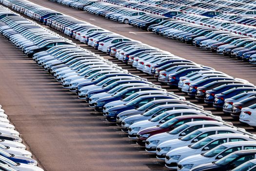 Rows of a new cars parked in a distribution center on a car factory on a sunny day. Parking in the open air.