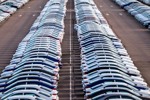 Rows of a new cars parked in a distribution center on a car factory on a sunny day. Top view to the parking in the open air.