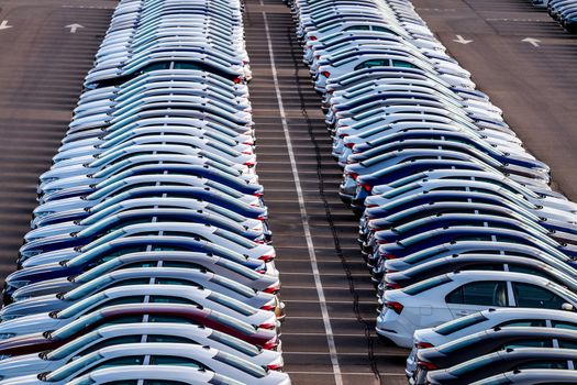 Rows of a new cars parked in a distribution center on a car factory on a sunny day. Top view to the parking in the open air.