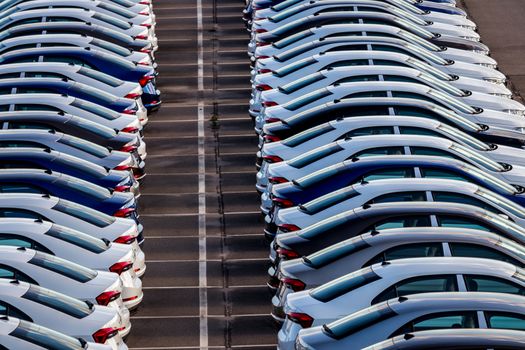 Rows of a new cars parked in a distribution center on a car factory on a sunny day. Top view to the parking in the open air.