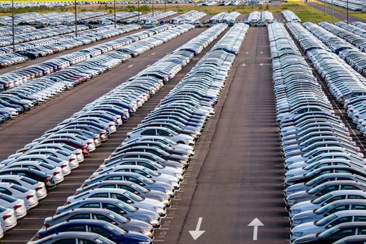 Rows of a new cars parked in a distribution center on a car factory on a sunny day. Top view to the parking in the open air.